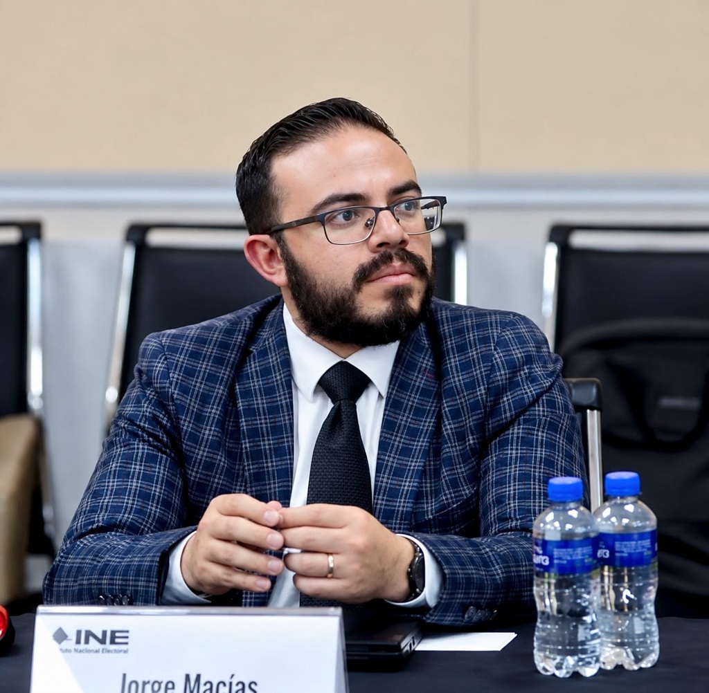 hombre de barba y lentes sentado con traje azul a cuadros