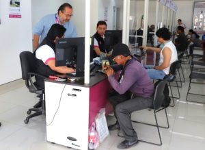 cuatro personas sentadas realizando trámites mientras un hombre los observa