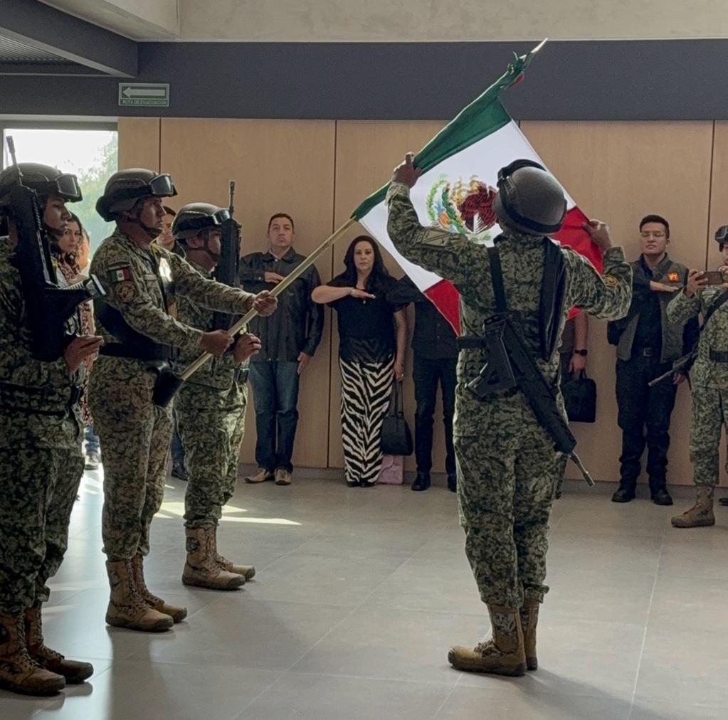 tres militares en fila horizontal sosteniendo la bandera nacional