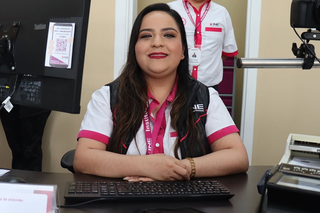 una mujer cabello largo sentada con brazos sobre la mesa y sonriendo