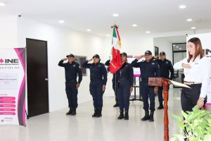 cinco personas uniformadas de pie en línea horizontal sosteniendo la bandera nacional
