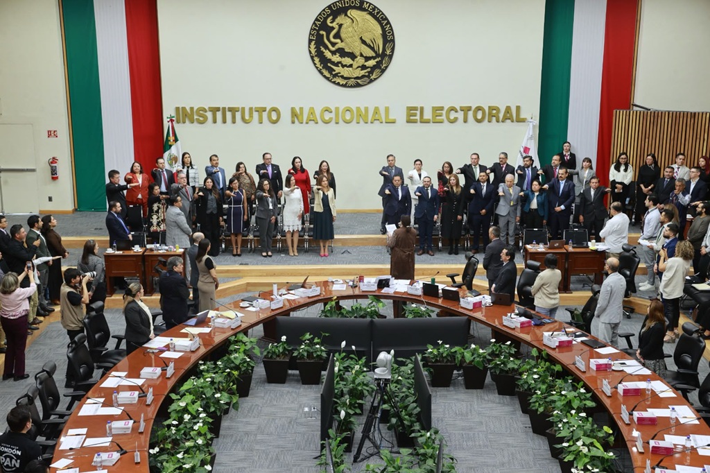 muchas personas de pie en un salón con el brazo derecho extendido al frente