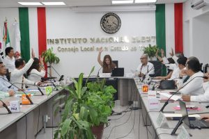 personas en un salón blanco sentadas, votando a mano alzada