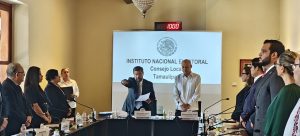 varias personas de pie, enmedio un hombre leyendo y con el brazo extendido hacia enfrente