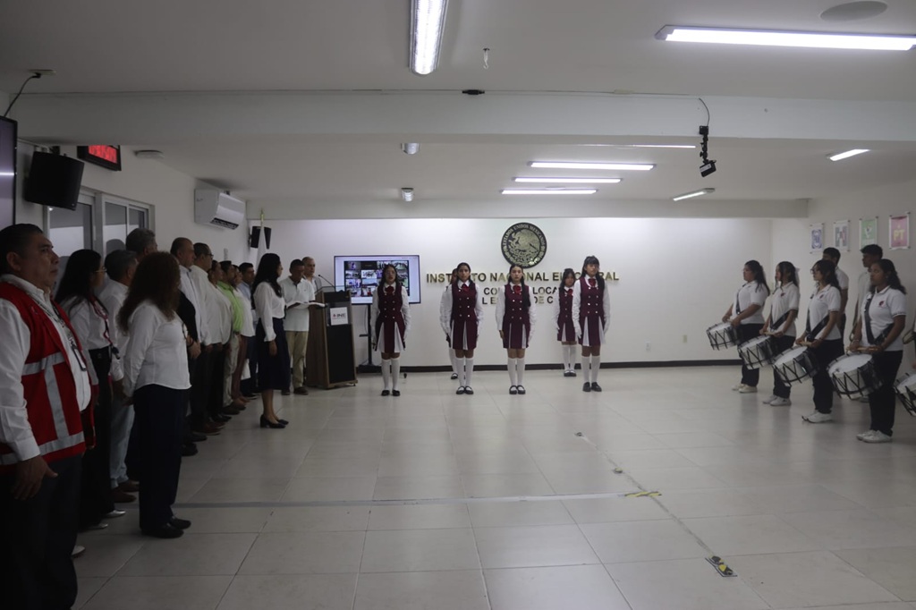 cinco estudiantes uniformadas de pie en línea horizontal sosteniendo la bandera nacional