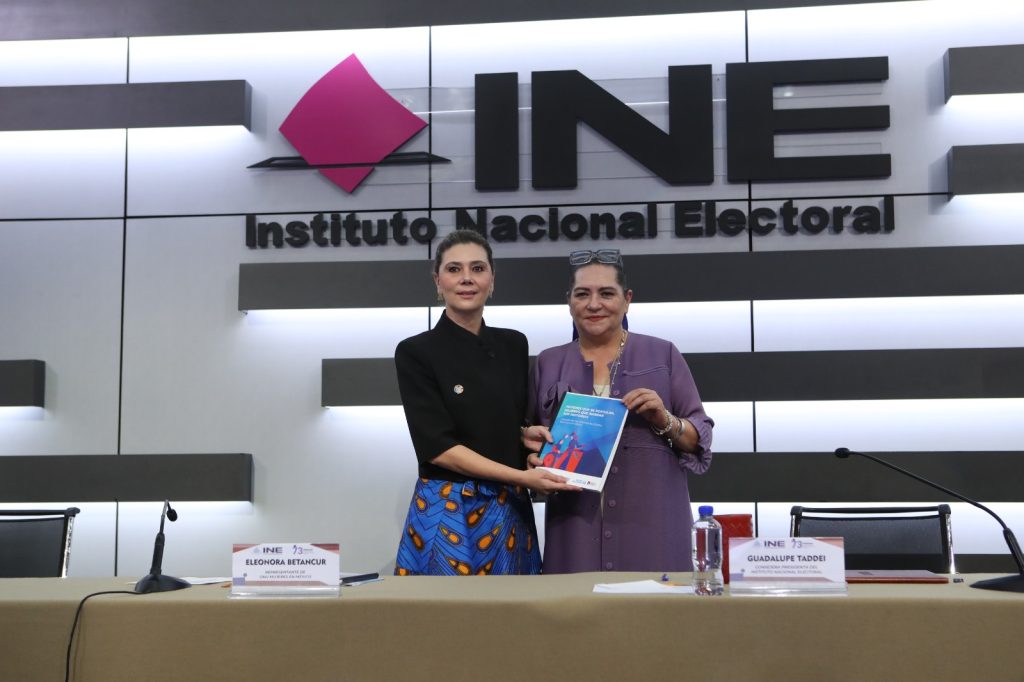 Guadalupe Taddei Consejera Presidenta del INE y Eleonora Betancur González, Representante de ONU Mujeres en México paradas en el estrado con la publicación en las manos.