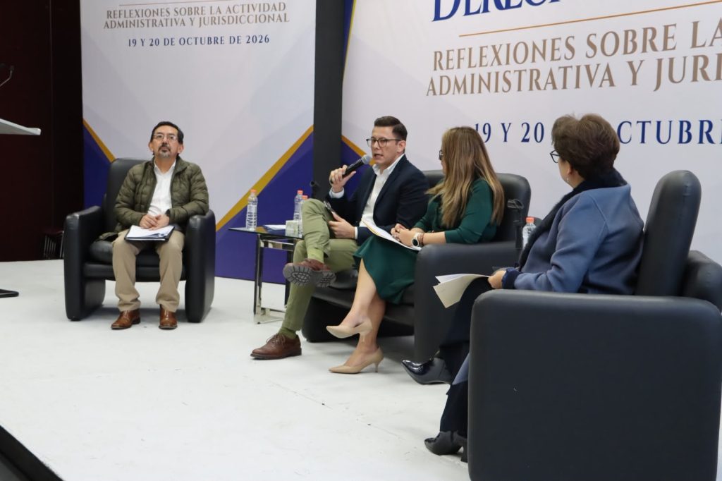 Hombre hablando en un escenario don dos mujeres y otro hombre
