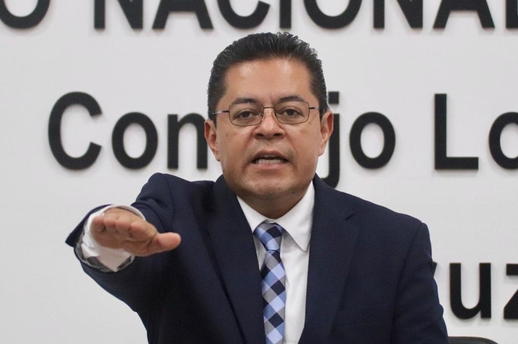 un hombre de lentes y traje negro con el brazo derecho extendido al frente