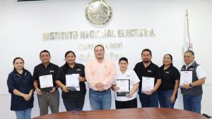 ocho personas de pie, abajo de un escudo nacional y letras doradas
