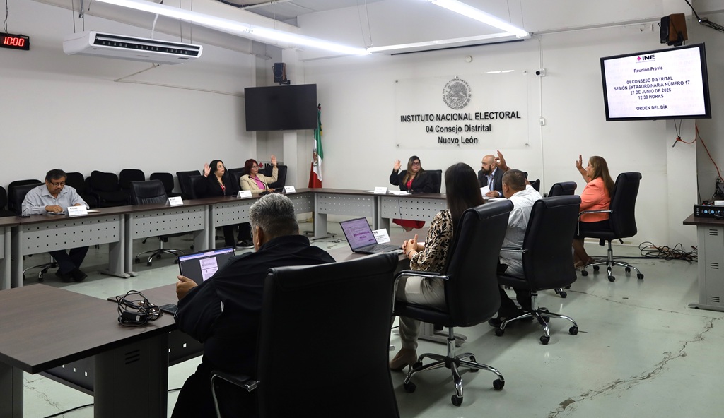 nueve personas en un salón sentadas y votando a mano alzada