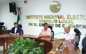 tres hombres sentados alrededor de una mesa de madera con micrófonos