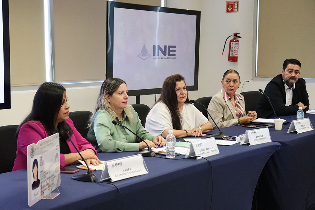 cuatro mujeres y un hombre sentados frente a una mesa con mantel gris