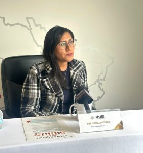 mujer sentada en sillón negro con saco a rallas grises y blancas