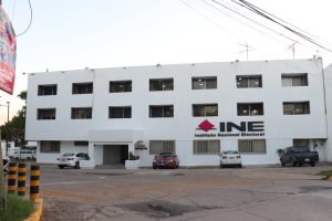 Edificio blanco de tres pisos con letras negras afuera que dicen INE